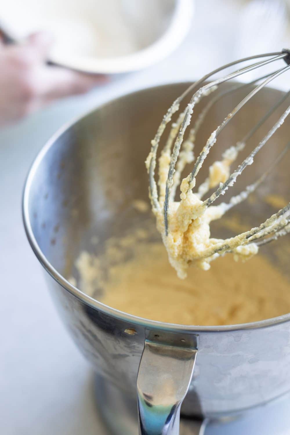 yellow cake batter on the whisk attachment of a silver stand mixer