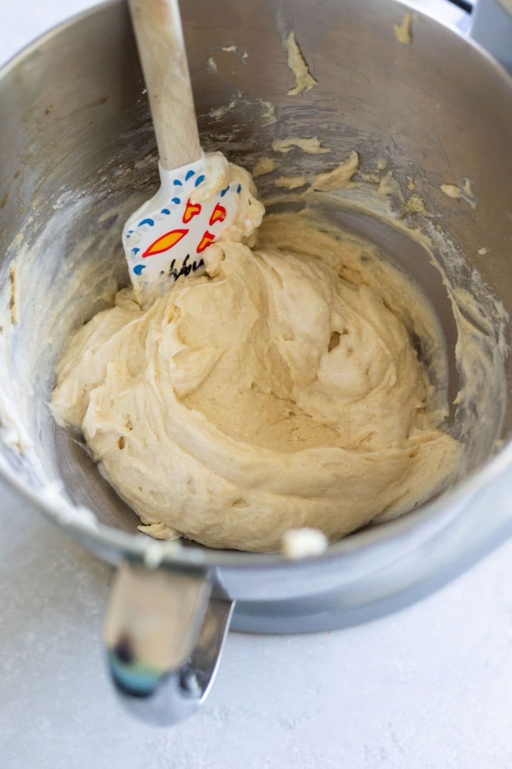 yellow cake batter in a silver mixing owl with a wooden rubber spatula sticking out