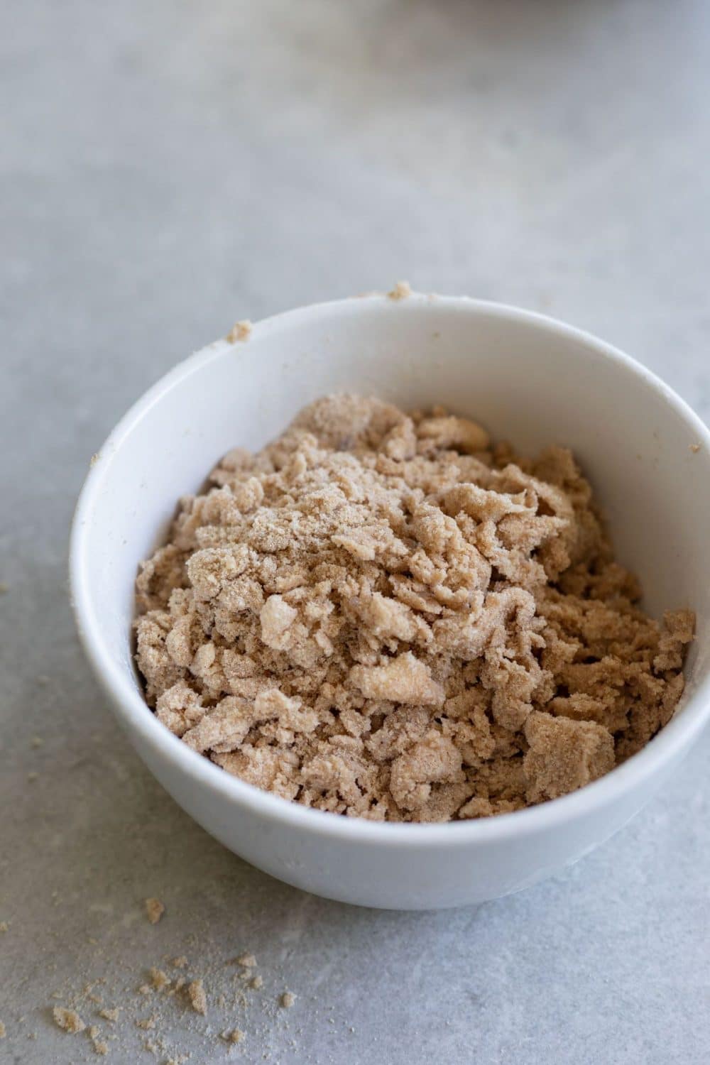 light brown streusel crumble in a white bowl on a grey counter