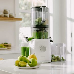 Nama J2 juicer with green juice and vegetables on a white counter.
