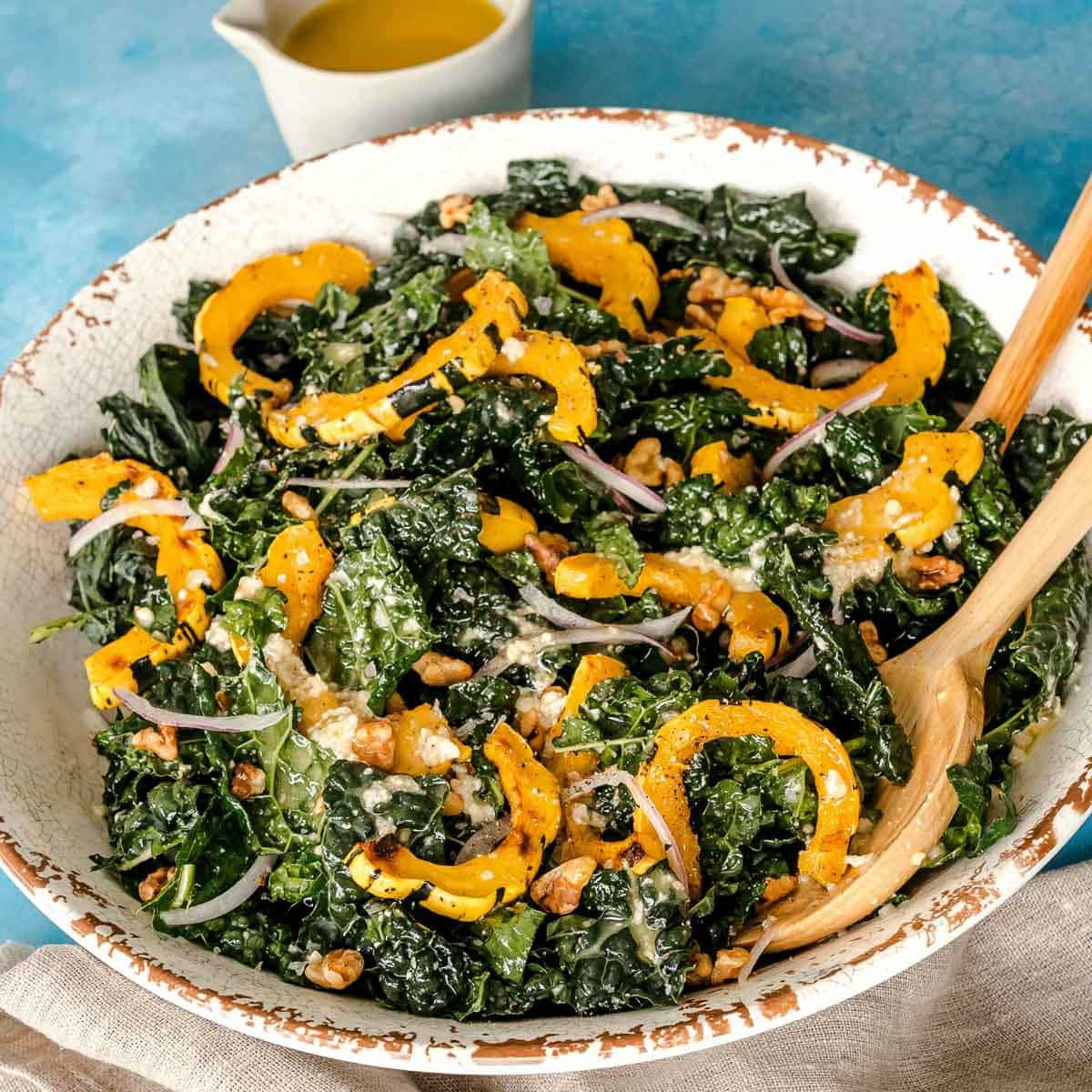 Kale and Delicata Squash salad with red onions in a salad white bowl on a blue counter.